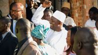 Valkoisiin pukeutunut hymyilevä Adama Barrow heiluttaa kättään. Ympärillä on useita ihmisiä.