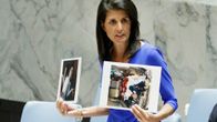 Nikki Haley seisoo kokouspöydän takana ja pitää käsissään kahta valokuvaa.