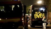 Kuva pommi-iskun kohteena olleesta jalkapallojoukkueen bussista. On ilta. Bussin takaosassa lukee suurin keltaisin kirjaimin "Heja BVB!" Etualalla kulkee nainen ja puhuu puhelimeen.