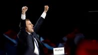 Tummaan pukuun pukeutunut Macron tuulettaa nyrkit ilmassa.