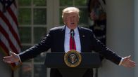 Trump puhujapöntössä valkoisen talon pihalla, levittelee käsiään. 