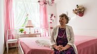Lyyli Vassinen istumassa vaaleanpunaisen sävyisessä makuuhuoneessaan.