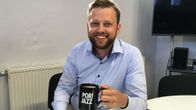 Mies hymyilee ja pitää kädessään Pori Jazz -kahvikuppia.
