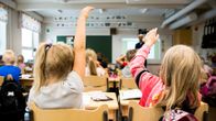 Kaksi lasta etualalla viittaavat oppitunilla.