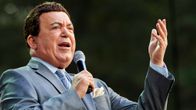 Harmaaseen pukuu pukeutunut Kobzon laulaa mikrofoniin ja elehtii vasemmalla kädellään.