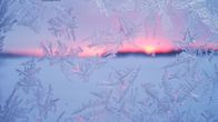 Jäähiutaleita ikkunassa ja takana auringonlasku.