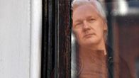 Julian Assange katselee ulos ikkunalasin takaa.