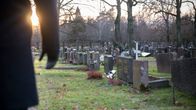 Mies on hautausmaalla ja katselee hautakiviä. Hän seisoo kuvan vasemmassa laidassa ja hänestä näkyy vain osa vartaloa ja oikea käsi. Laskeva talvinen aurinko pilkottaa käden kainalosta.
