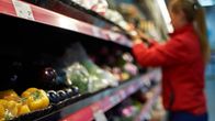 Työntekijä täyttää vihanneshyllyä supermarketissa.
