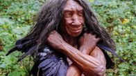 Hymyilevä pitkätukkainen neandertalialaisnanen painaa ison linnun siipiä olkapäitään vasten. 