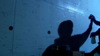 Silhouettimainen hahmo pyyhkii seinää hämärässä valossa.