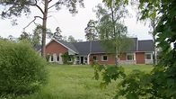 Vanhainkodin rakennus ja pihaa: matala harjakattoinen rakennus, puita ja pensaita.
