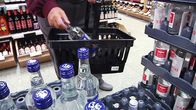 Asiakas siirtää viinapulloa ostoskoriin Alkossa.