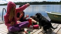 Lapset pistävät koiran tassuihin vauhtia kesäisellä laiturilla.