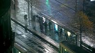 Ihmisiä sateessa raitiovaunupysäkillä.
