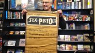 Mies esittelee Sex Pistolsin keikkamainosta Epesin myymälässä
