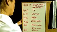 Hoitaja etualalla pitelee taulua, johon on kirjoittettu päivän aikataulu (vessa, vaipat ja aamiainen, TV, lounas, kahvi, vessa ja vaipat, päivällinen, vessa, vaipat ja iltapala).