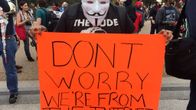 Guy Fawkes -naamiolla varustautunut mielenosoittaja pitelee kylttiä, jossa lukee "Älä huoli, olemme internetistä".