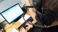Mies istuu tietokoneen äärellä headset-luurit päässään