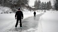 Mies ja nainen luistelevat luistelureitillä joen jäällä.