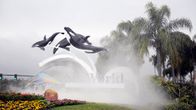 Kolme muovista miekkavalasta ponnistaa ilmaan SeaWorldin mainoksessa palmujen katveessa.
