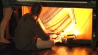 Nainen istuu pianon edessä, jonka sisukset on paljastettu. Hän soittaa pianoa pianon sisältä.
