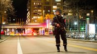 Aseistettu poliisi seisoo keskellä katua, kaukana näkyy hälytysajoneuvojen valoja.