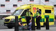 Ensihoitaja tutkii kadulla istuvaa miestä. Vierellä kaksi poliisia. Taustalla ambulanssi.