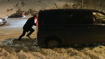 Mies työntää lumeen juuttunutta pakettiautoa liikkeelle.