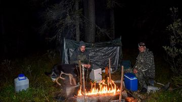 Kaksi miestä ja koira iltanuotiolla