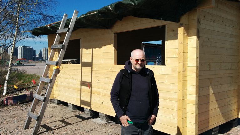 Rakennustöitä vetävä Matti Kinnunen seisoo uuden hirsisaunan edessä aurinkolasit päässä.