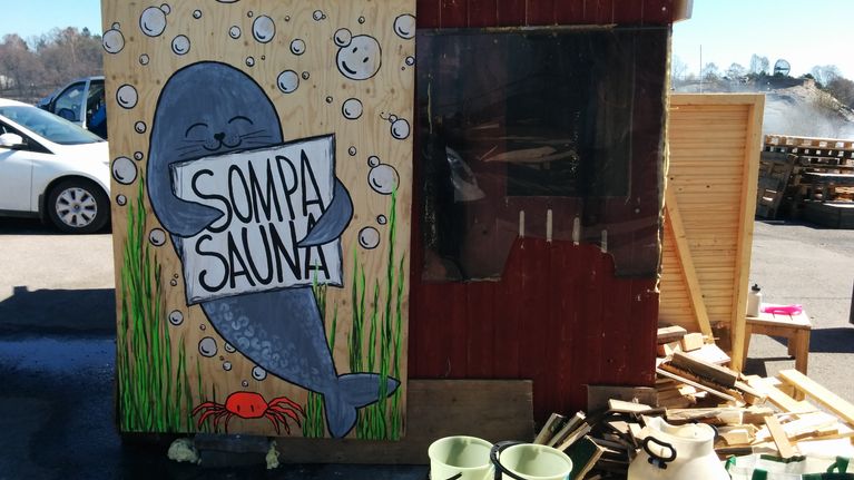 Maalauksessa hylje pitää sylissään kylttiä, jossa lukee "Sompasauna"