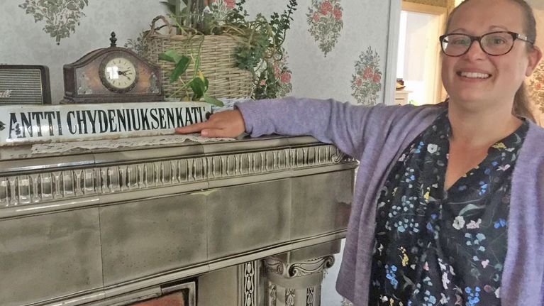 Jutta Piispanen seisoo kodissaan ja esittelee pelastamaansa vanhaa katukylttiä.