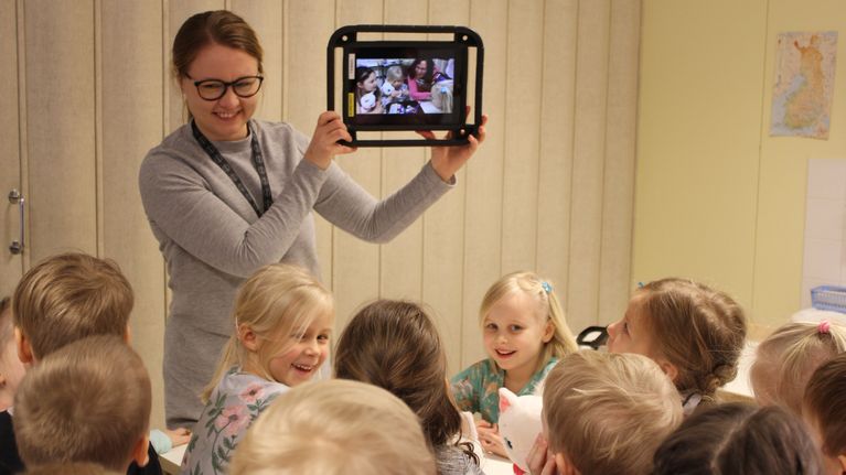 Kotkan varhaiskasvatuksen kehittämiskoordinaattori Tiina Kääpä näyttää lapsille näiden keksimää tarinaa tabletin näytöltä.