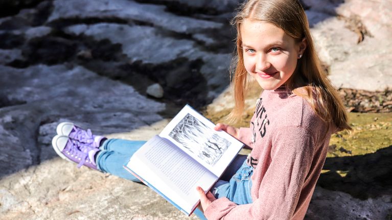 Olivia Lorien Levo istuu ja pitelee Hobitti-kirjaa.