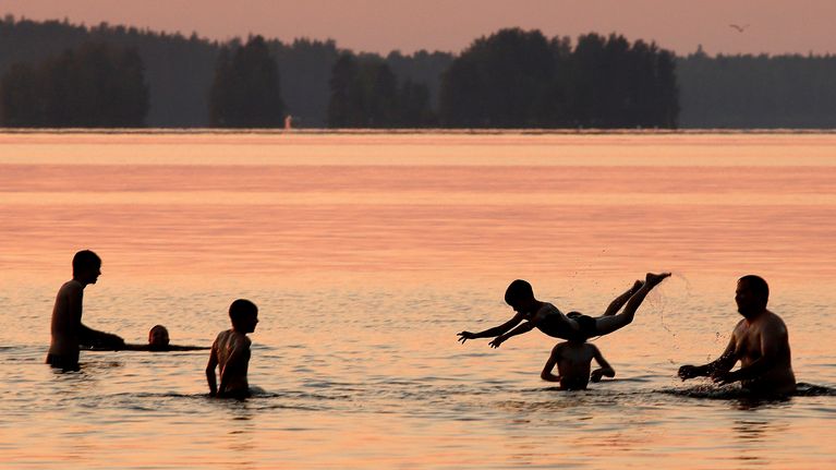 Aikuisia ja lapsia uimassa auringonlaskun aikaan.