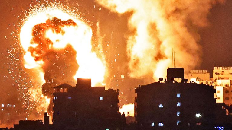 Kuvassa nousee lieskoja Gazan kaistaleelta. Etualalla näkyy rakennuksia, joiden takana on lieskoja. 