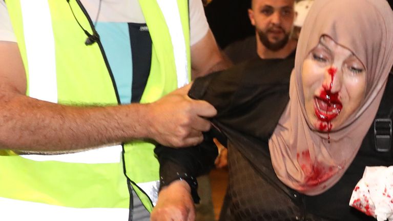 Kuvassa mies taluttaa haavoittunutta palestiinalaisnaista. Huivipäisen naisen kasvoista vuotaa verta. 