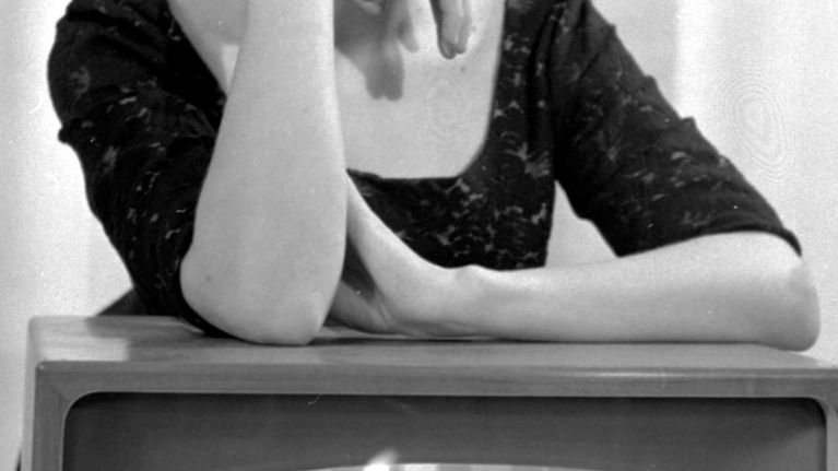  Kuuluttaja Teija Sopanen nojaa televisiovastaanottimeen. Televisio on auki ja siinä näkyy taukokuva. 1959