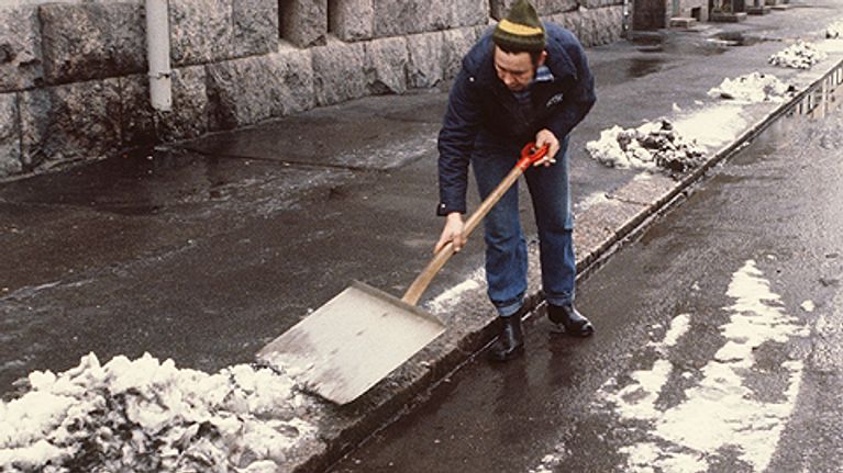 Mies lapioi loskaista lunta jalkakäytävältä.