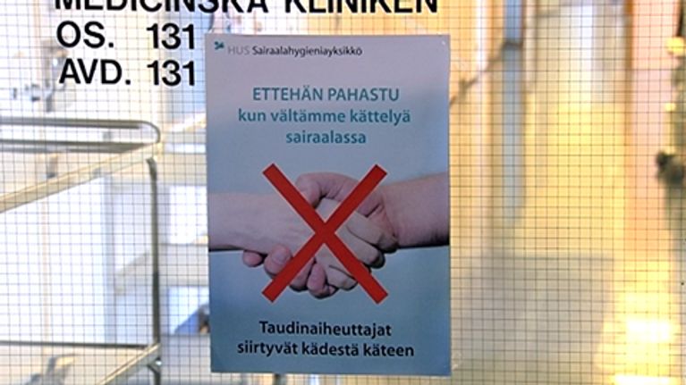 Juliste sairaalan ovessa varoittaa taudinaiheuttajien leviämisestä kättelyn kautta.