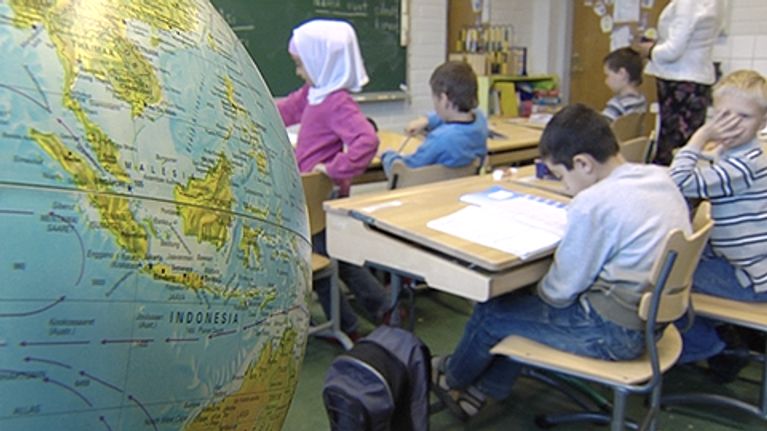 Oppilaita ala-asteen luokkahuoneessa, kuvan etualalla karttapallo.
