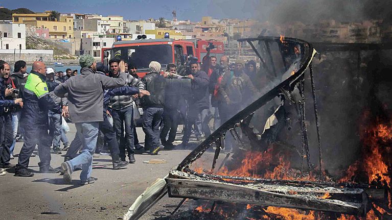 Edustalla palava asuntovaunu, ja taustalla tunisialaisia siirtolaisia.