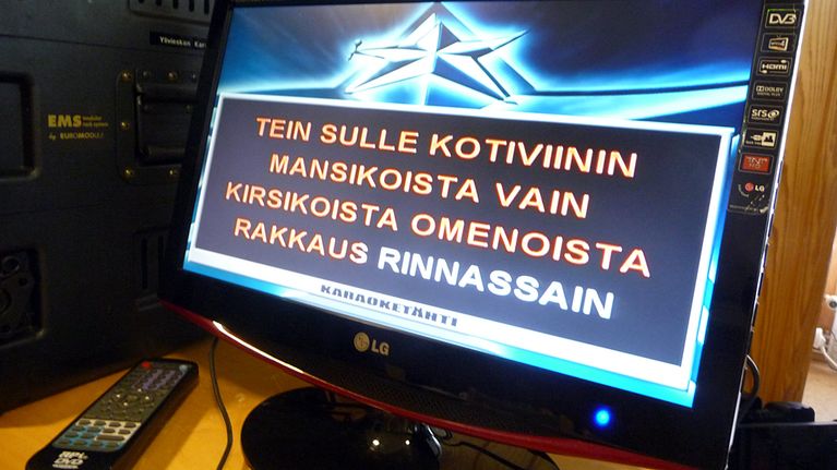 Lähikuvassa karaokelaitteen näytöllä kotiviini-kappaleen sanoja.