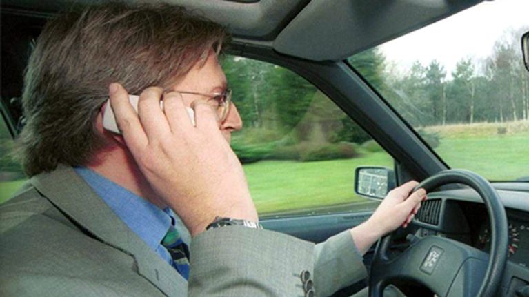 Mies ajaa autoa kännykkä korvalla.