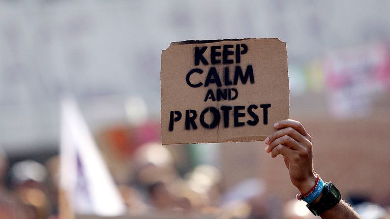 Mielenosoittaja pitelee "Pysykää rauhallisena ja protestoikaa" -kylttiä.