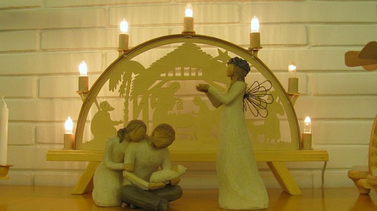 Puusta veistetyt Maria ja Joosef Jeesus-lapsen kanssa vierellään enkeli. Taustalla puinen kynttelikkö. 