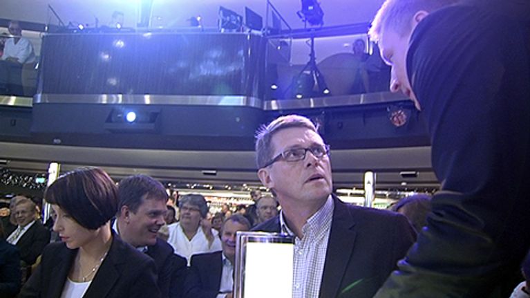 Kansanedustaja Kimmo Tiilikainen puhuu puolueen puheenjohtajalle, pääministeri Matti Vanhaselle laivan yökerhossa, johon puolueen väkeä on kokoontunut istumaan. Taustalla puoluesihteeri Jarmo Korhonen.