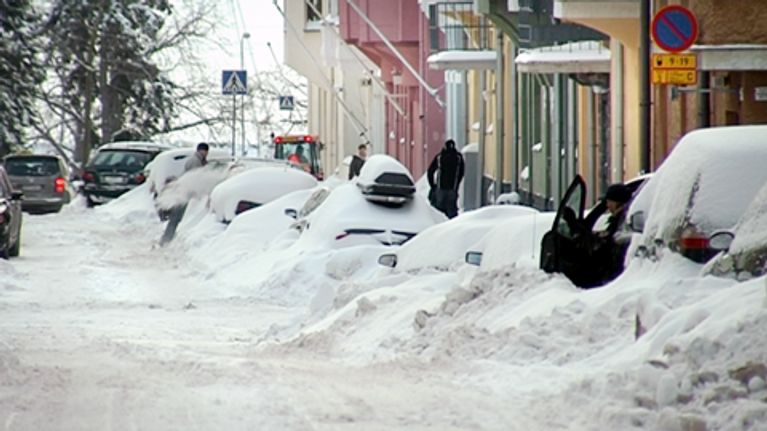 Lumen peitossa olevia autoja kadun varrella Helsingissä.