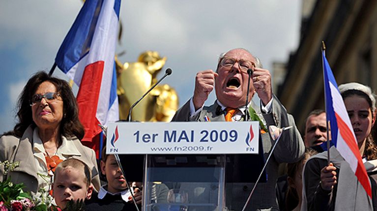 Ranskalaispoliitikko Jean-Marie Le Pen laulaa Ranskan kansallislaulua äärioikeistolaisen Front Nationalin puoluekokouksessa. Eläytyy ja pitää käsiään koholla nyrkissä. Vierellään nuoria lapsia ja taustalla Ranskan lippu.
